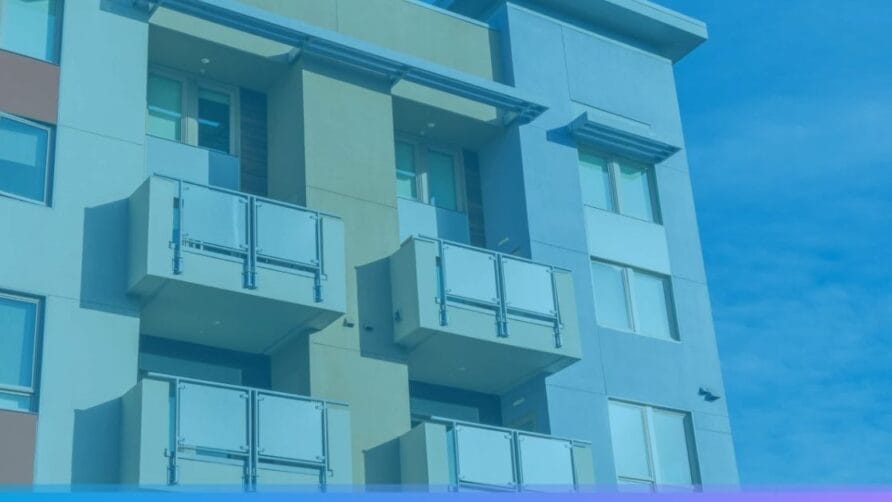 Modern apartment building with multiple balconies and large windows against a clear blue sky.