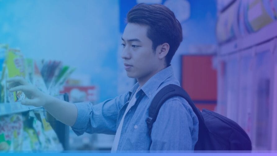 Person shopping in a grocery store aisle, reaching for an item on a shelf with a backpack on their shoulder.