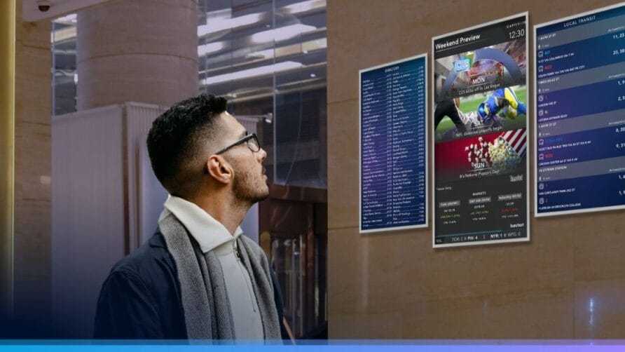 Man looking at digital sports display in a modern building lobby, featuring game previews and statistics.