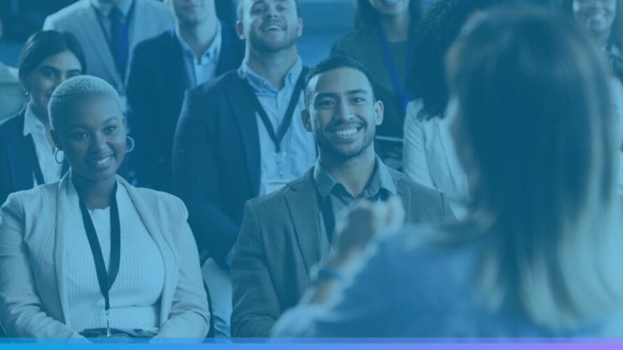 Audience smiling and listening to a speaker at a conference or seminar in a professional setting.