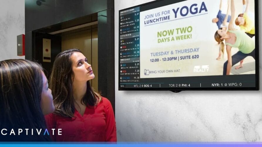 Two women looking at a screen displaying a yoga class advertisement in an indoor setting.