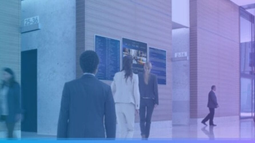 People walking in a modern office lobby with digital information screens on the wall.