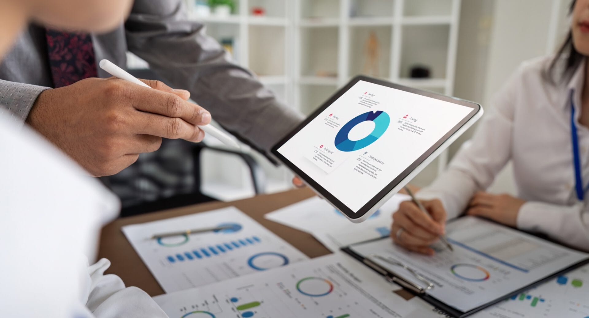 People analyzing financial charts on a digital tablet and paper documents in an office setting.