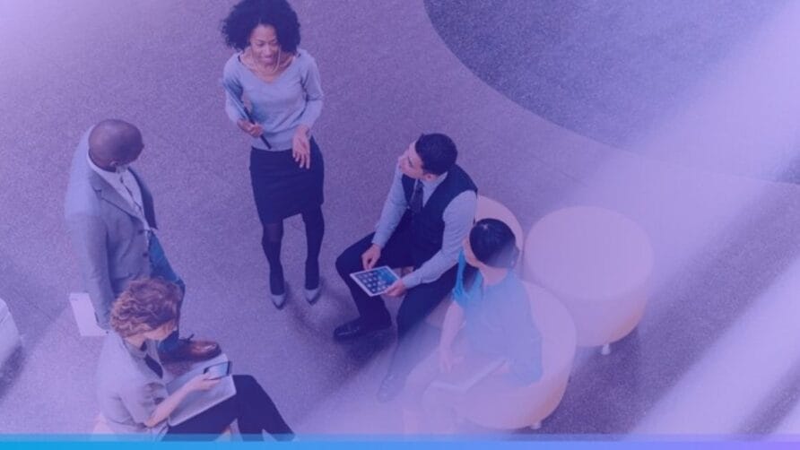 Colleagues having a discussion while sitting and standing in a modern office lobby setting.