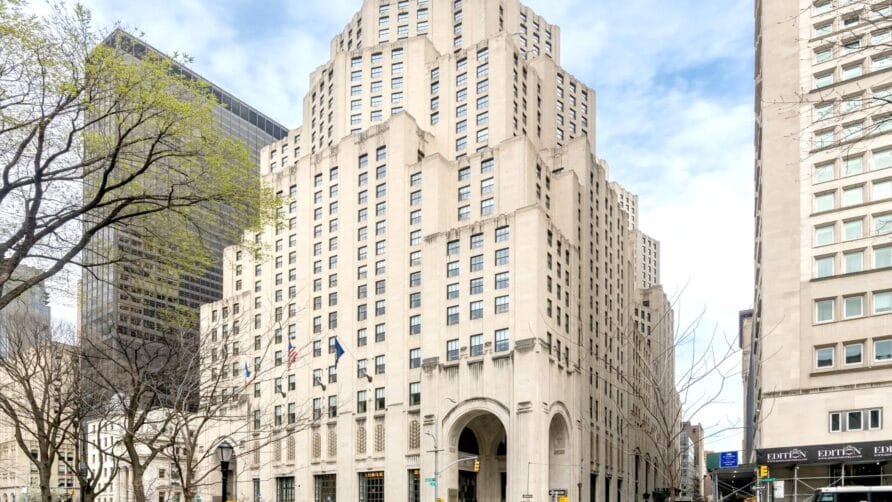 Art Deco skyscraper with detailed facade under a blue sky, trees and street in the foreground.