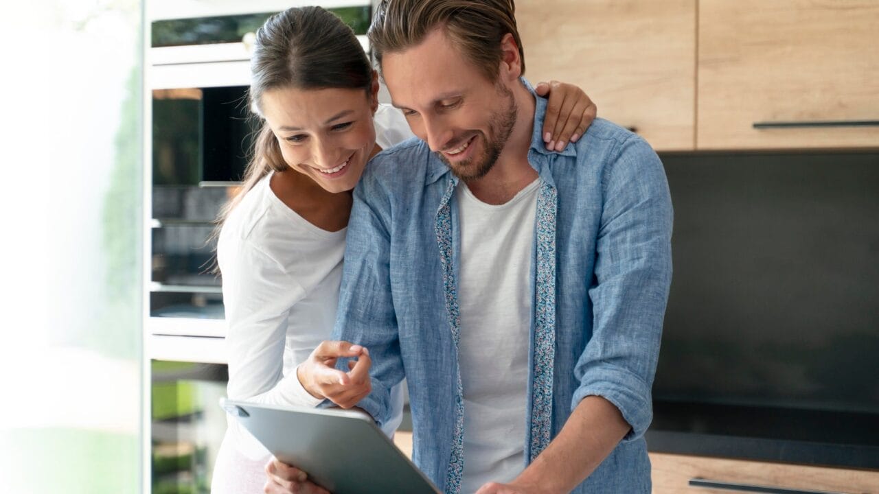 Couple happily looking at a tablet in a modern kitchen.