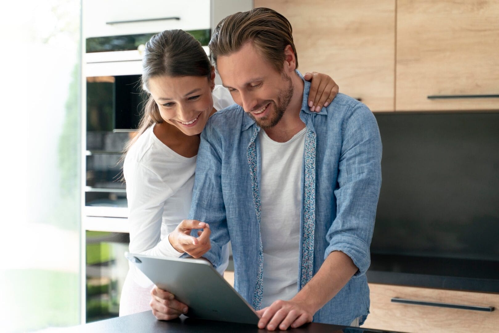 Couple happily looking at a tablet in a modern kitchen.