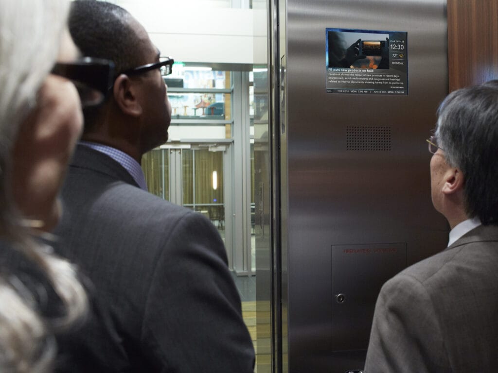 people ride an elevator and read the news and advertisements on the digital screen