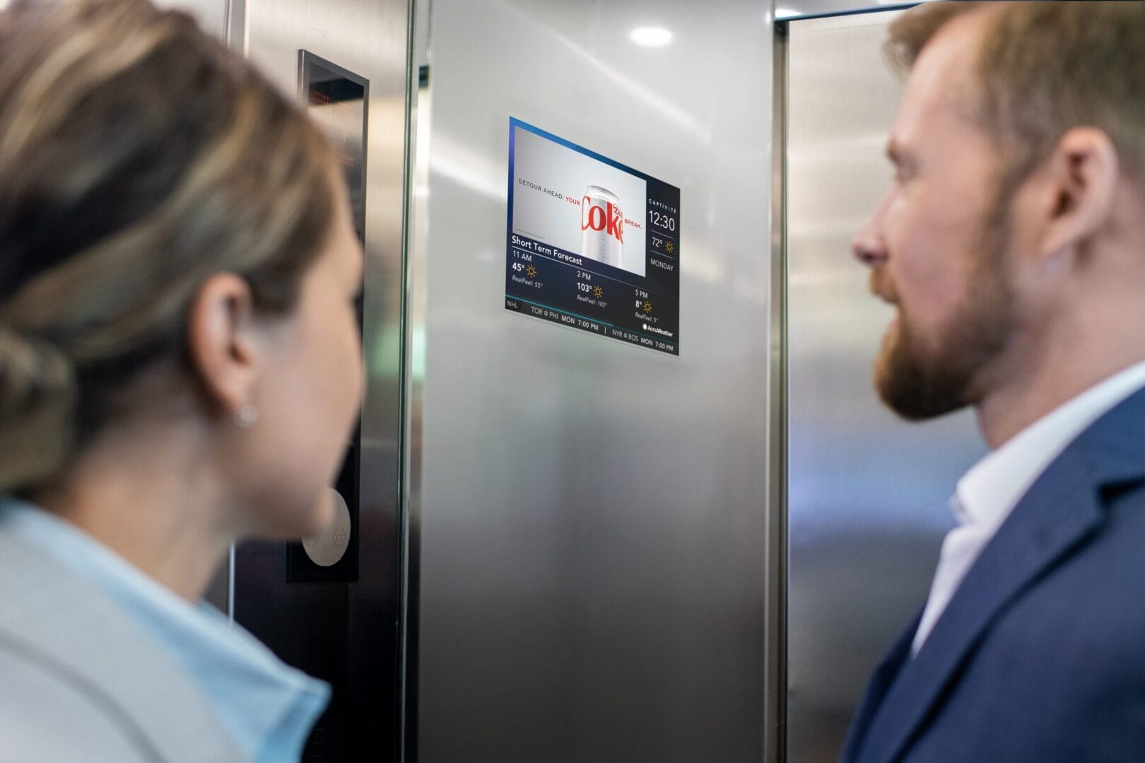 Two people looking at a monitor inside an elevator displaying a chart or graph.