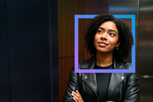 Woman in a leather jacket with curly hair, framed by a blue square, smiling and looking upward against a modern wooden background.