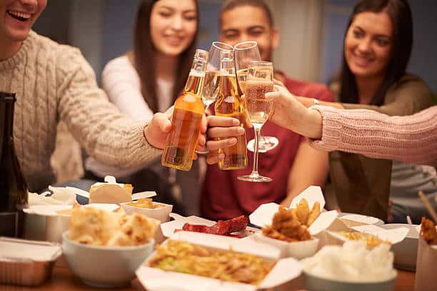 Friends toasting with drinks around a table filled with various food dishes.