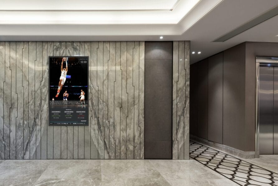 Modern lobby with marble walls, digital sign displaying an event, and intricate floor design.