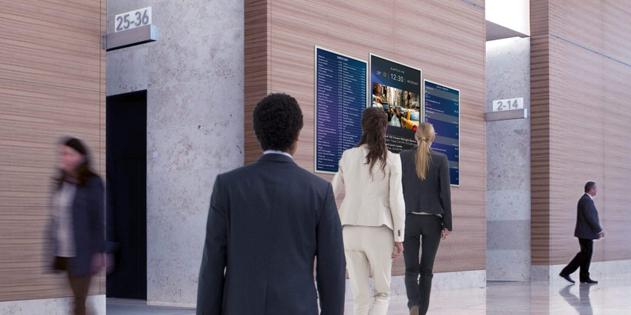 People in business attire walking towards digital displays on a modern office wall.