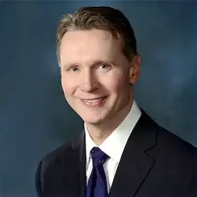 Man in a suit smiling against a blue background.