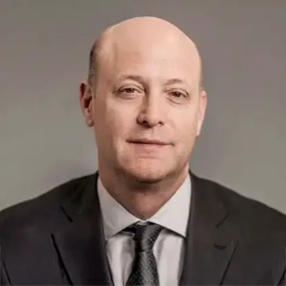 Bald man in a suit and tie with a neutral expression against a plain background.