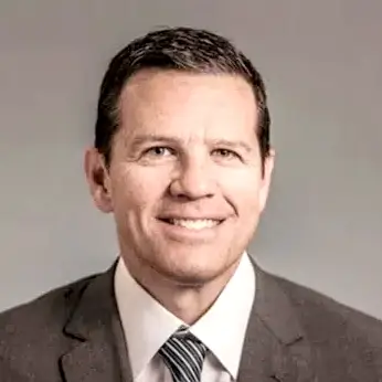 Man in suit and tie smiling against a plain background.