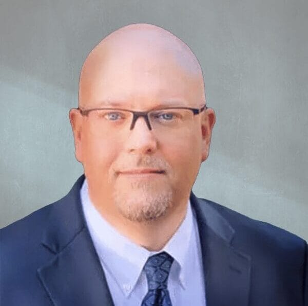 Bald man with glasses wearing a suit and tie against a neutral background.