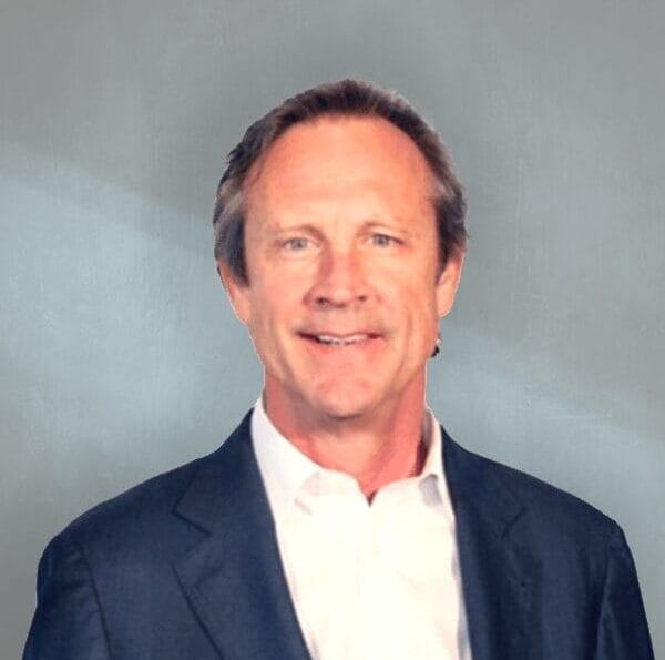 Smiling man in a suit with a blue background, business professional headshot.