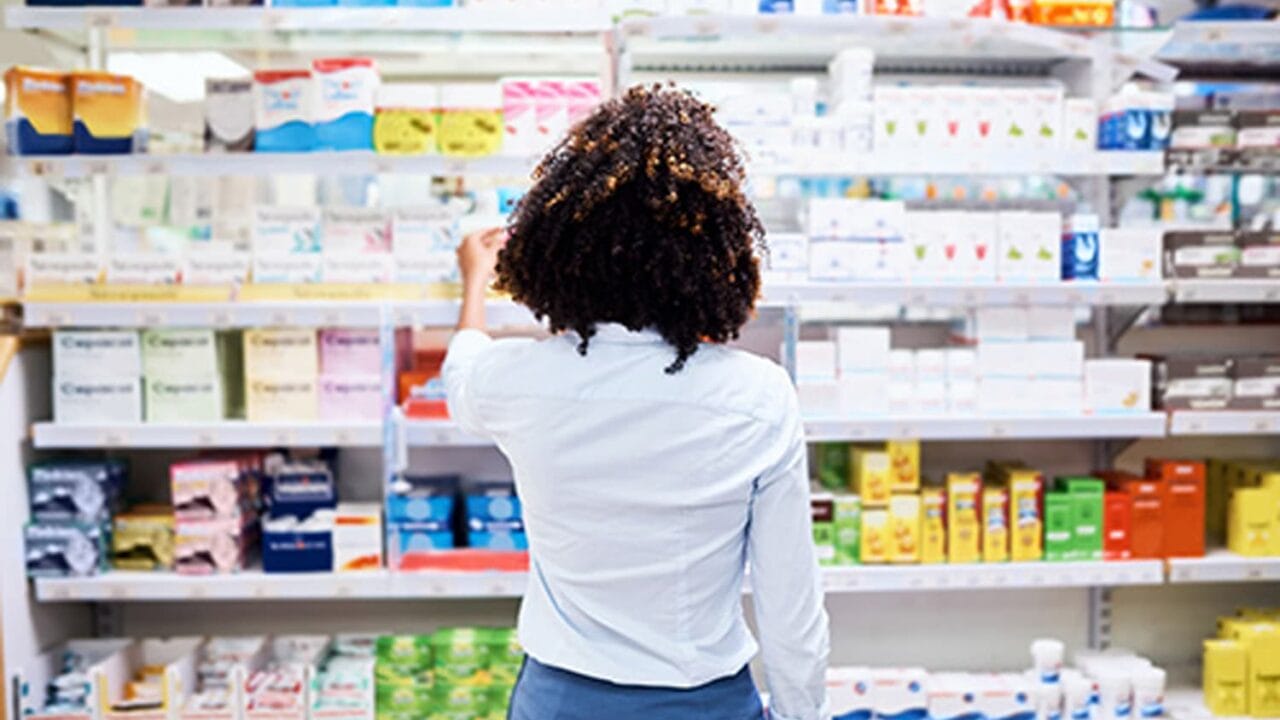 Person selecting a product from shelves in a pharmacy, surrounded by various medical and personal care items.