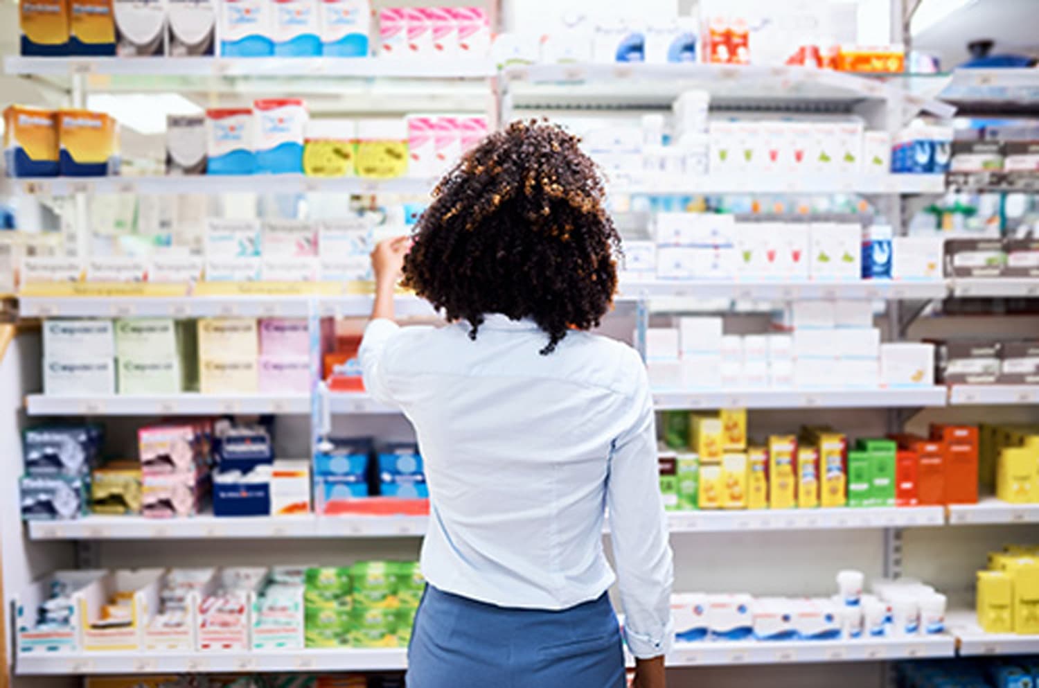 Person selecting a product from shelves in a pharmacy, surrounded by various medical and personal care items.