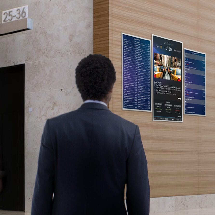 Person in a suit looking at large digital menu displays on a modern building wall.