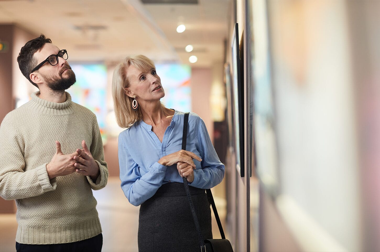 Two people viewing art in a gallery, examining a framed piece on the wall.