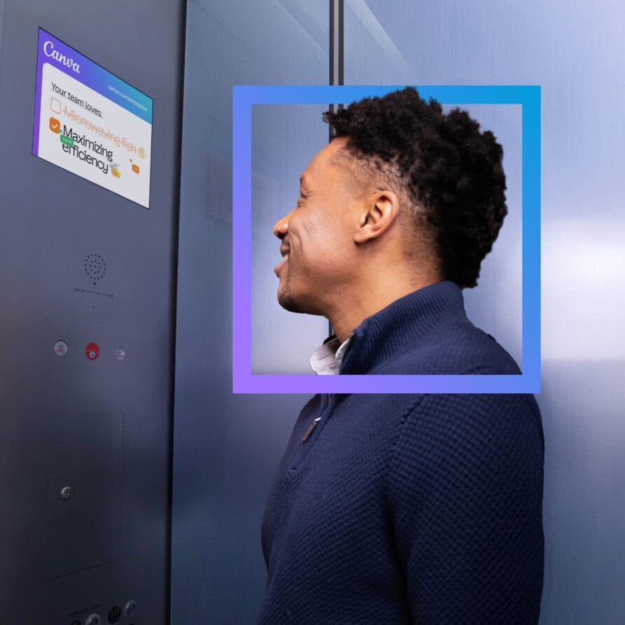 Man standing sideways with a blue frame around his head, looking at a screen on a metallic wall.