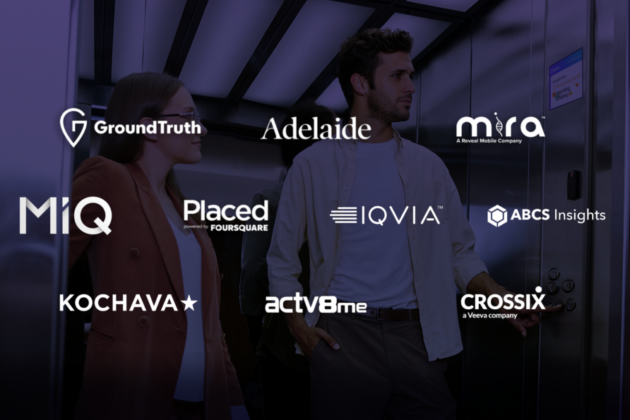 People walking past a display of various company logos, including Adelaide and Placed, in a modern, dimly lit environment.