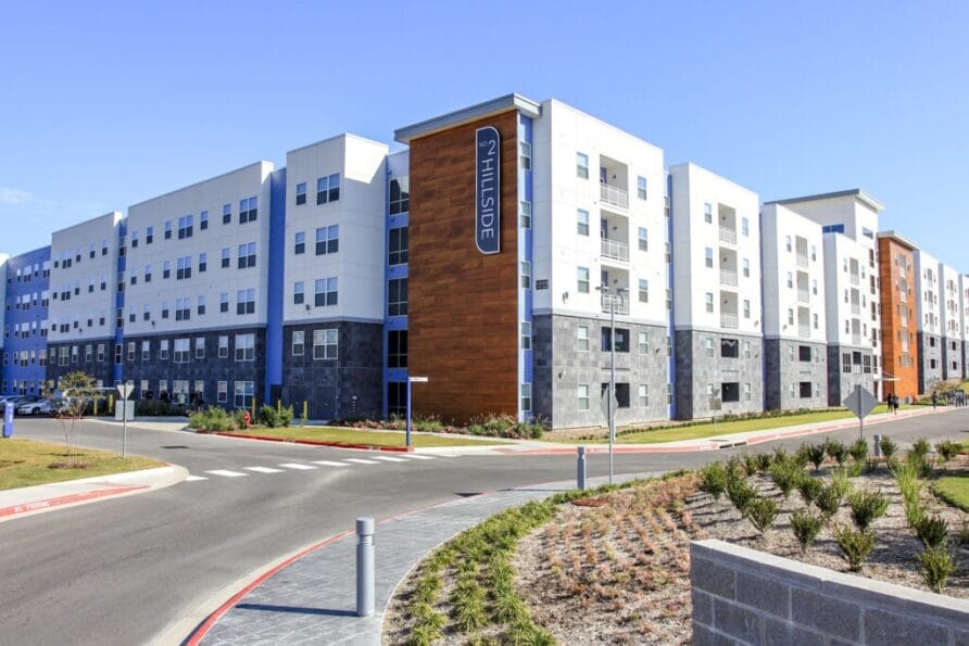 Modern four-story apartment building with a mix of white and brick exterior under a clear blue sky.