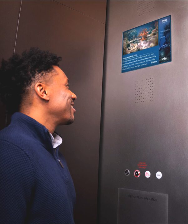Man in elevator looking at digital screen displaying underwater scene and Dell logo.