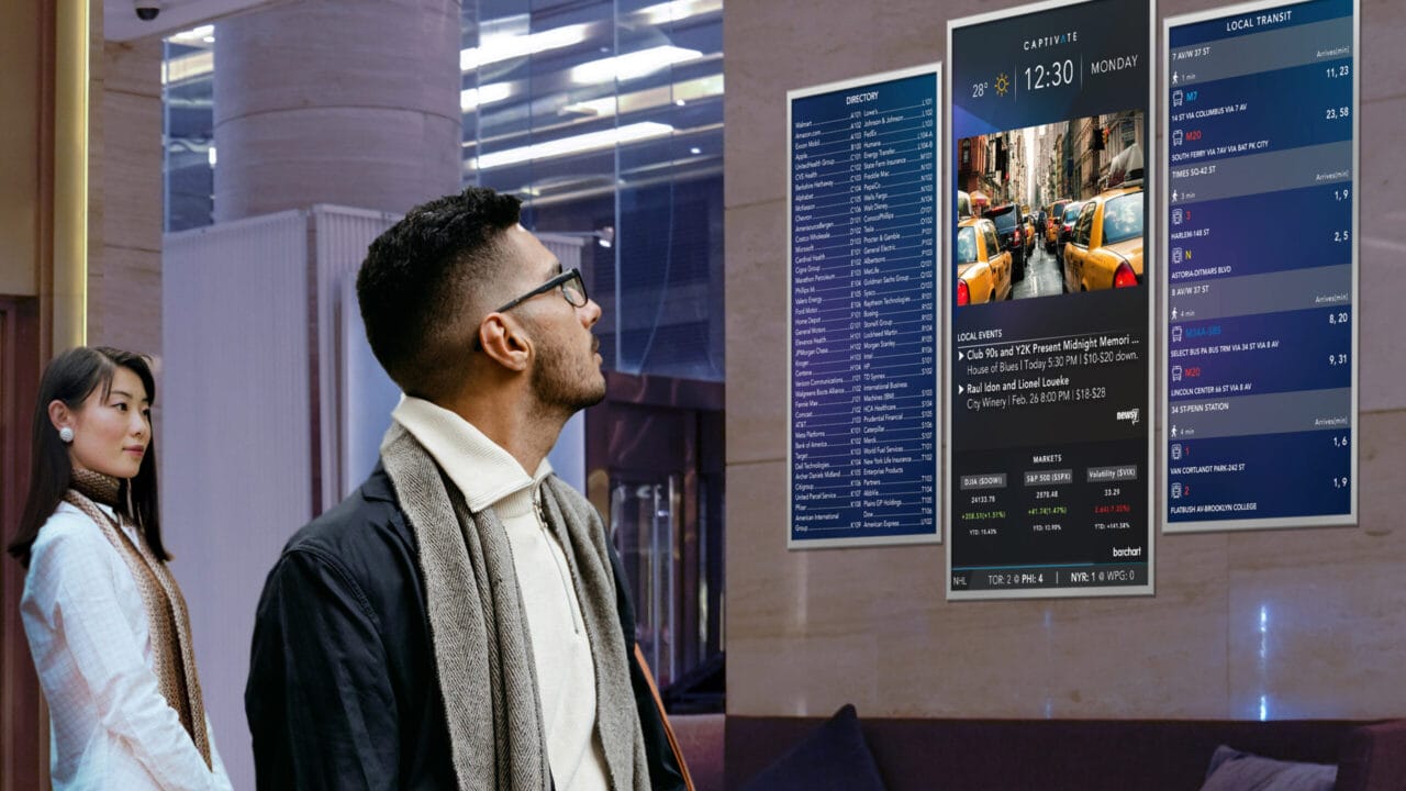 Man and woman looking at digital information displays in a modern lobby with list of events and transport details.