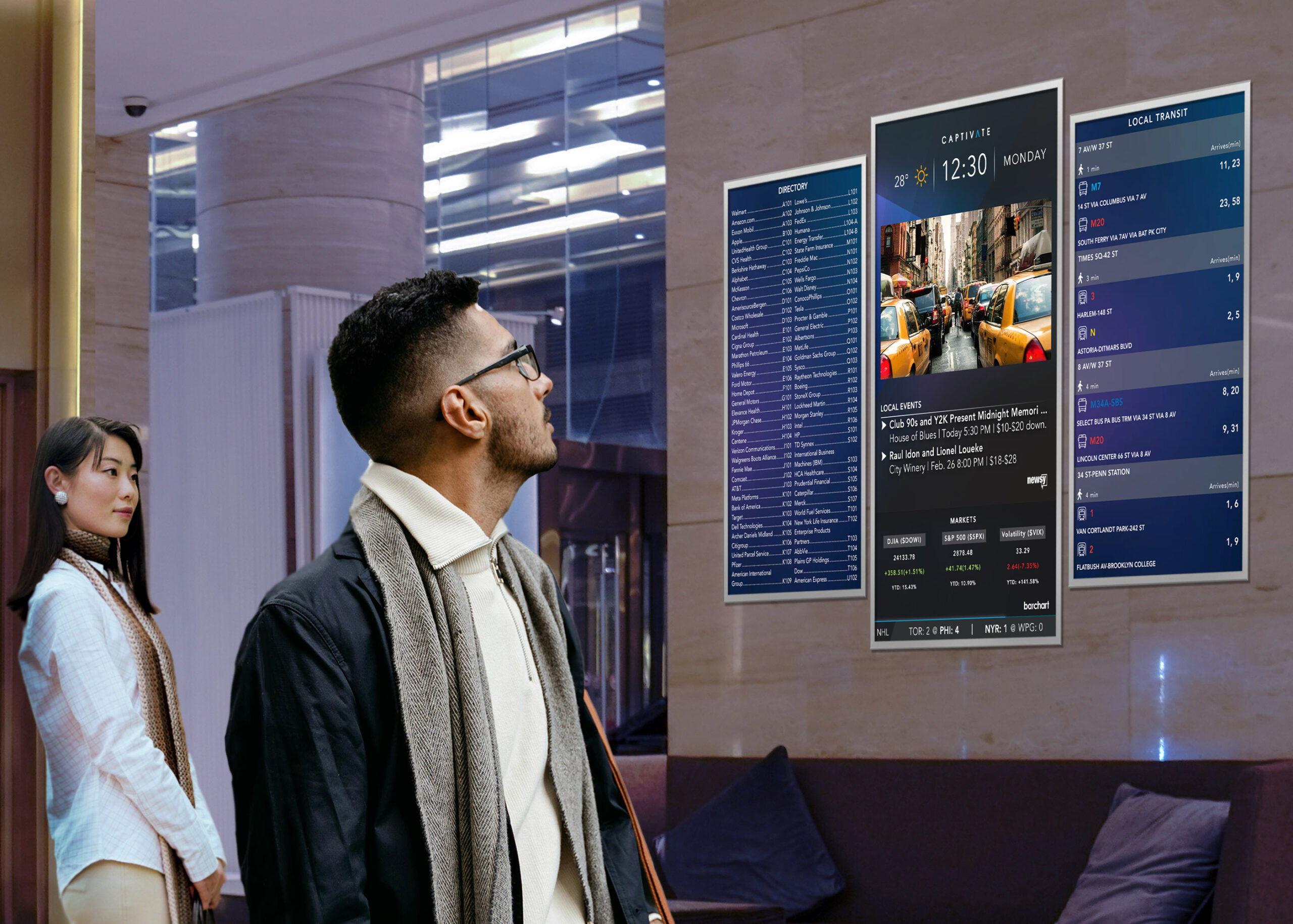 Man and woman looking at digital information displays in a modern lobby with list of events and transport details.