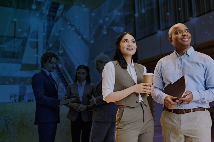 Professionals holding coffee and documents, standing in a modern office setting with colleagues in the background.