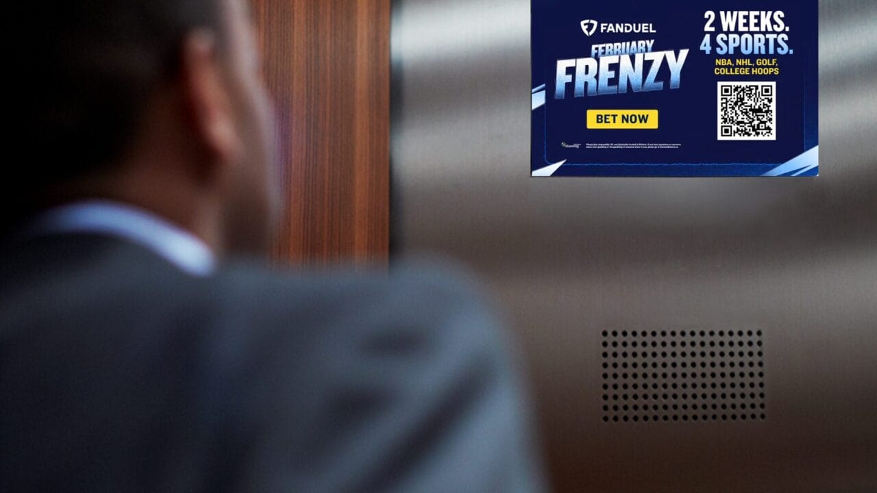 Man in suit looking at sports betting advertisement on digital screen inside an elevator.