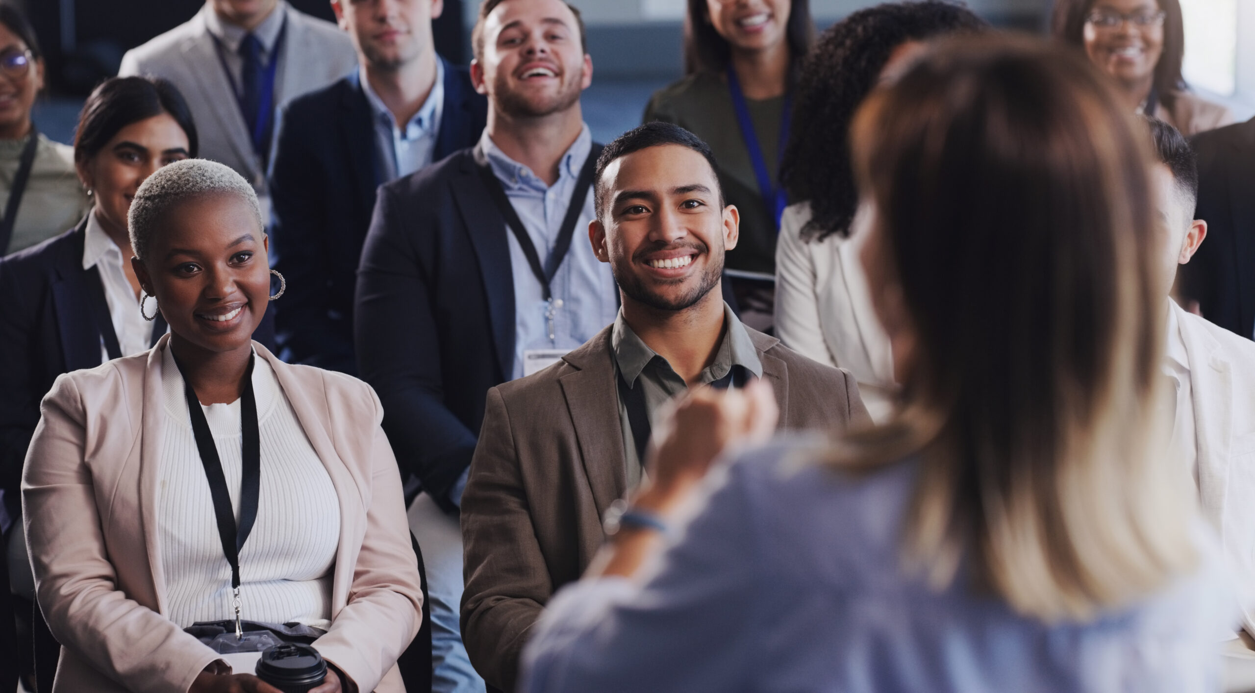 Diverse group of people smiling and listening to a speaker during a seminar or conference in a well-lit room.