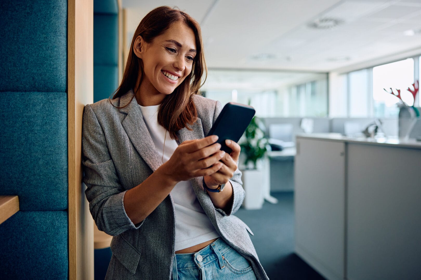 Woman smiling while using her smartphone in a modern office setting.