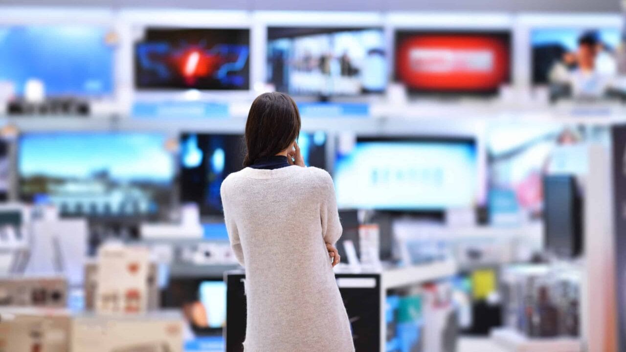 Woman in store browsing flat screen televisions on display, focused on various models and screens showing different images.