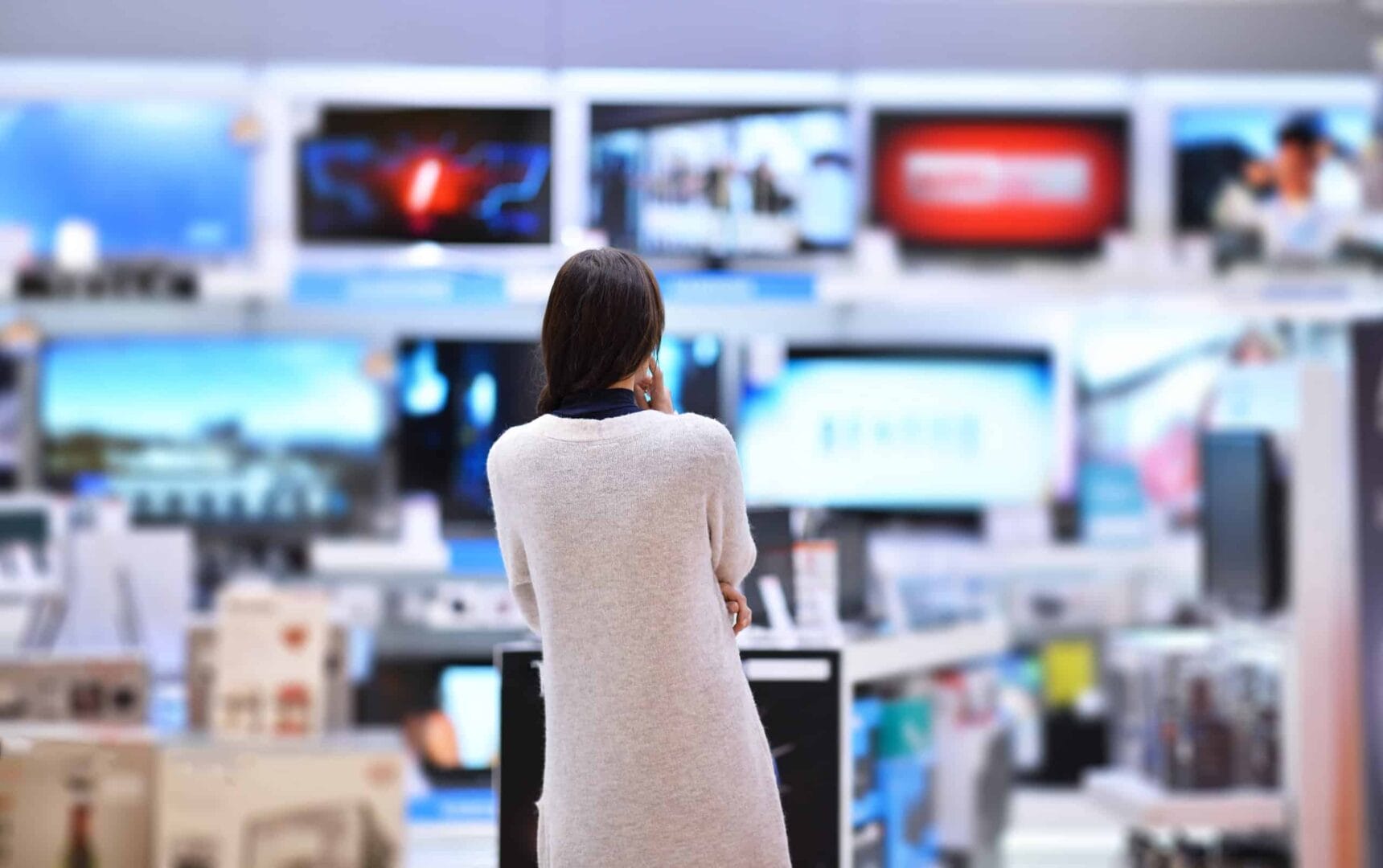 Woman in store browsing flat screen televisions on display, focused on various models and screens showing different images.