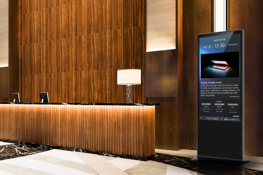 Hotel lobby with a wooden reception desk, a modern floor lamp, and an electronic display board.
