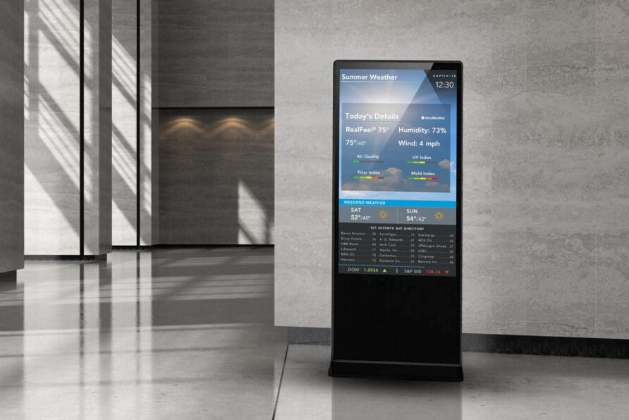 Digital information kiosk in a modern lobby displaying interactive content with sleek black design and illuminated screen.