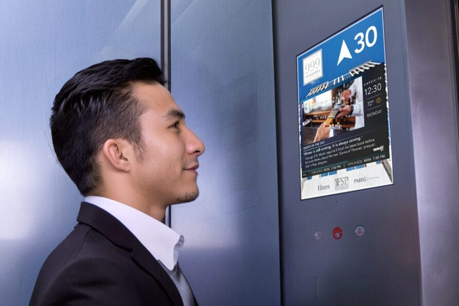 Man in suit looking at digital display screen with information in elevator.
