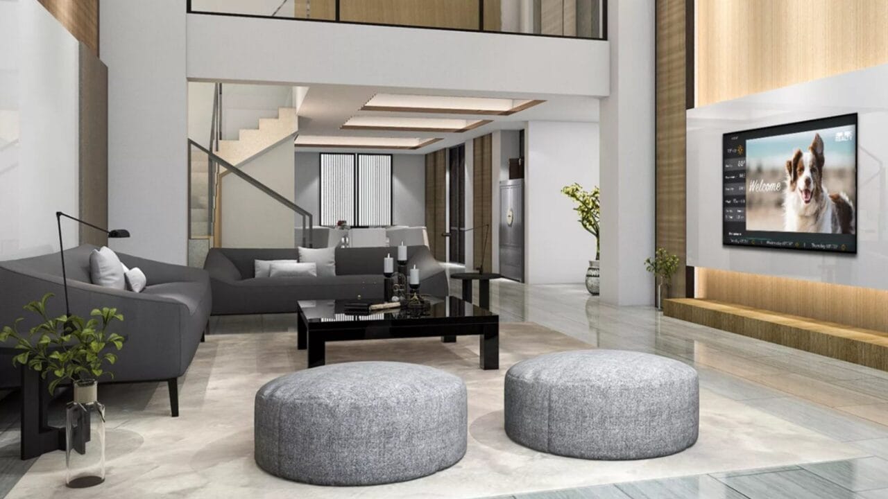 Modern living room with gray sofas, round ottomans, glass coffee table, TV on wall, and decorative plants.