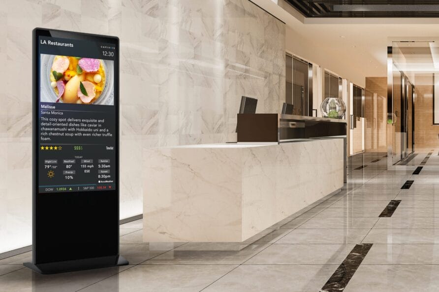 Digital menu board in a modern hotel lobby, next to a marble front desk and sleek interior design elements.