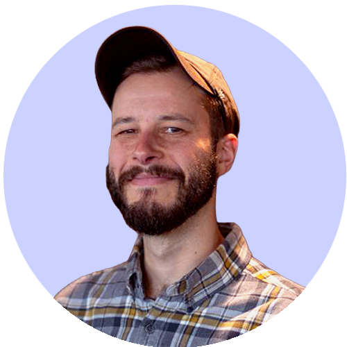 Man wearing a hat and plaid shirt smiling against a purple background.