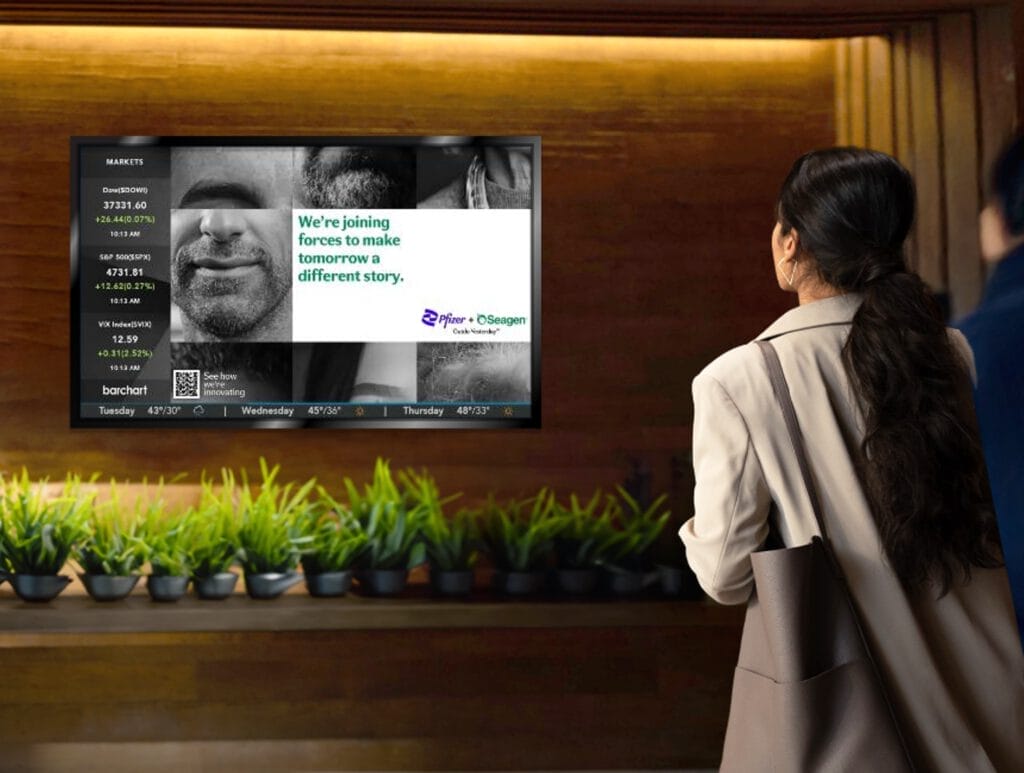 Person standing in front of a wall-mounted digital screen with green plants below the display.