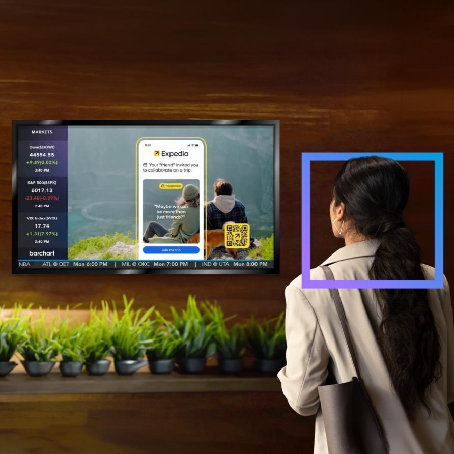 A person with a ponytail watching a screen displaying a business platform interface above a row of potted plants.