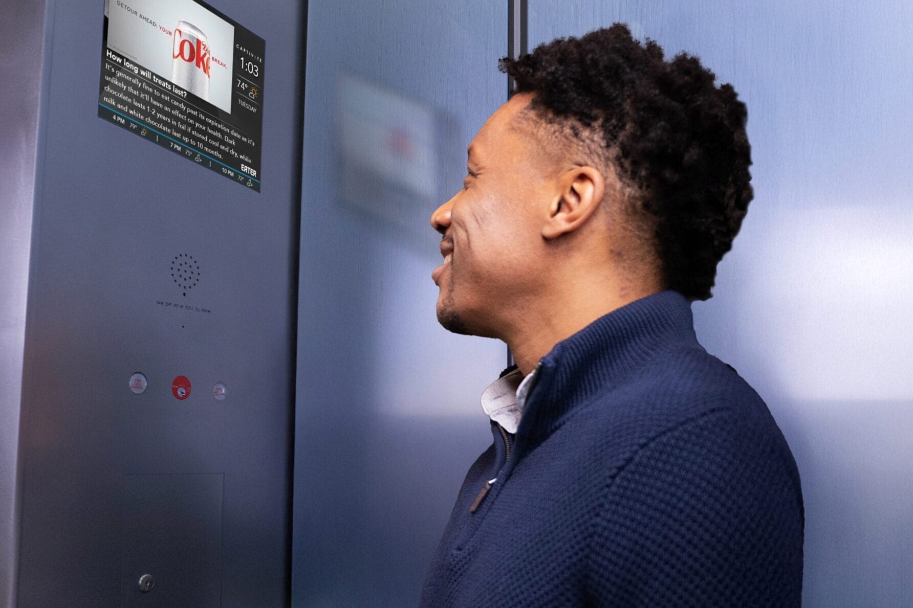 Person standing in front of an elevator, looking at the control panel with a screen and buttons.