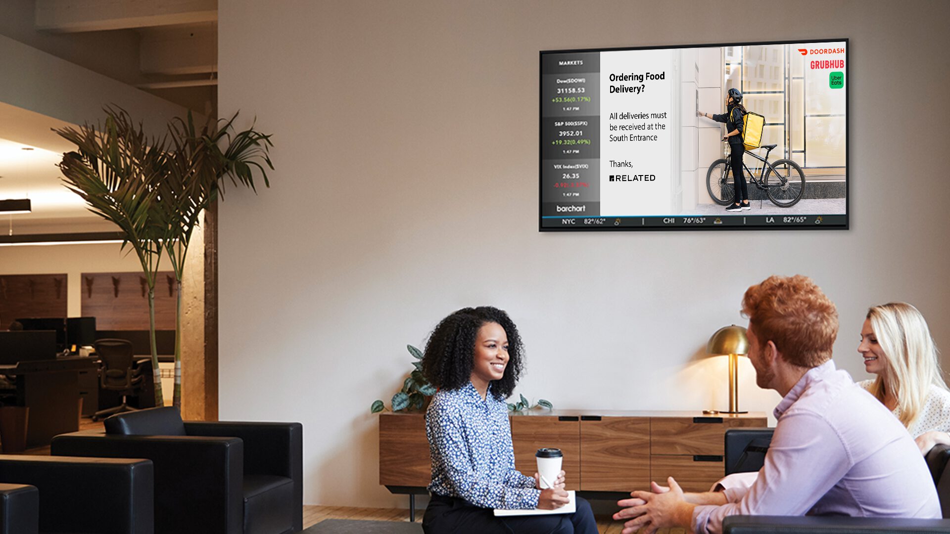 Three colleagues having a meeting in a modern office with a screen displaying delivery service information in the background.