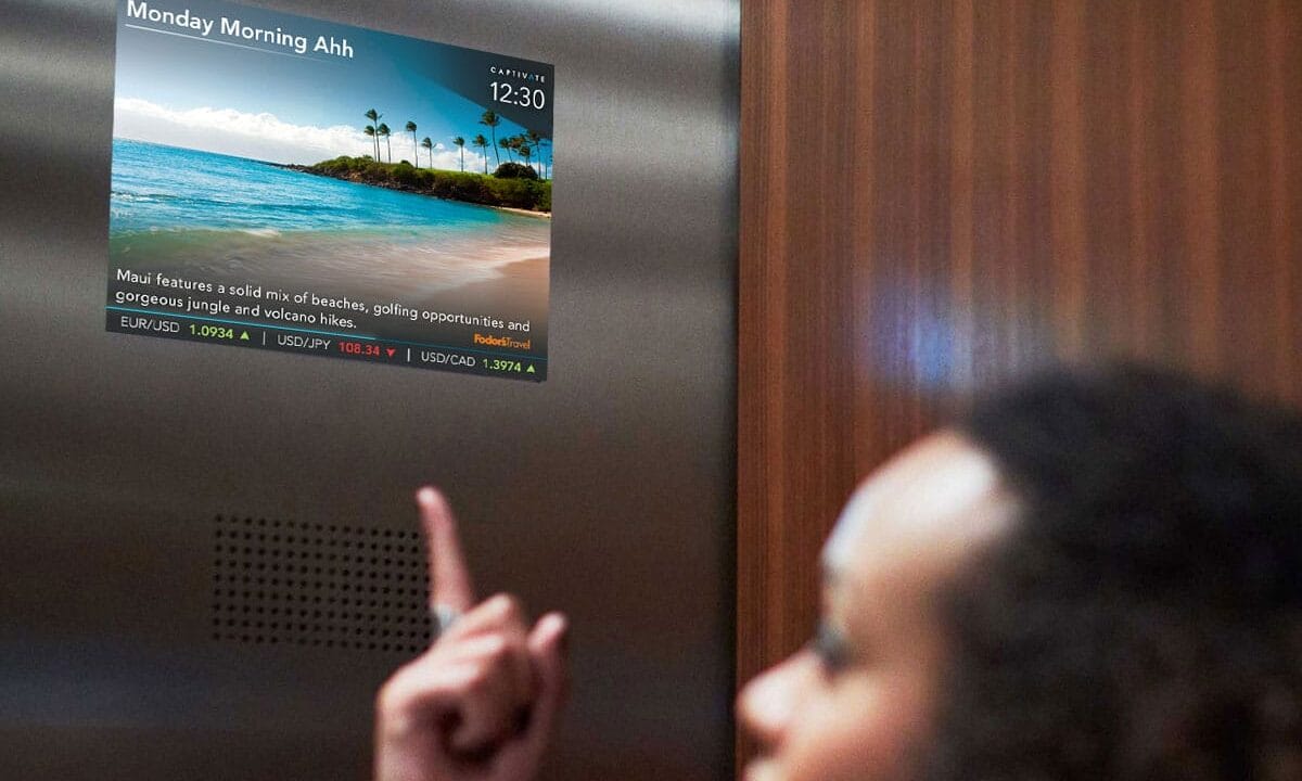 Person in elevator pointing at screen displaying scenic beach image and financial data.