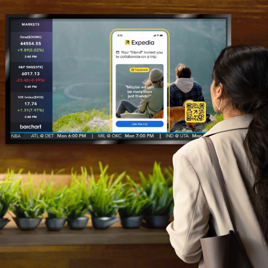 Woman watching a digital display with a travel app advertisement, surrounded by green plants in a modern setting.